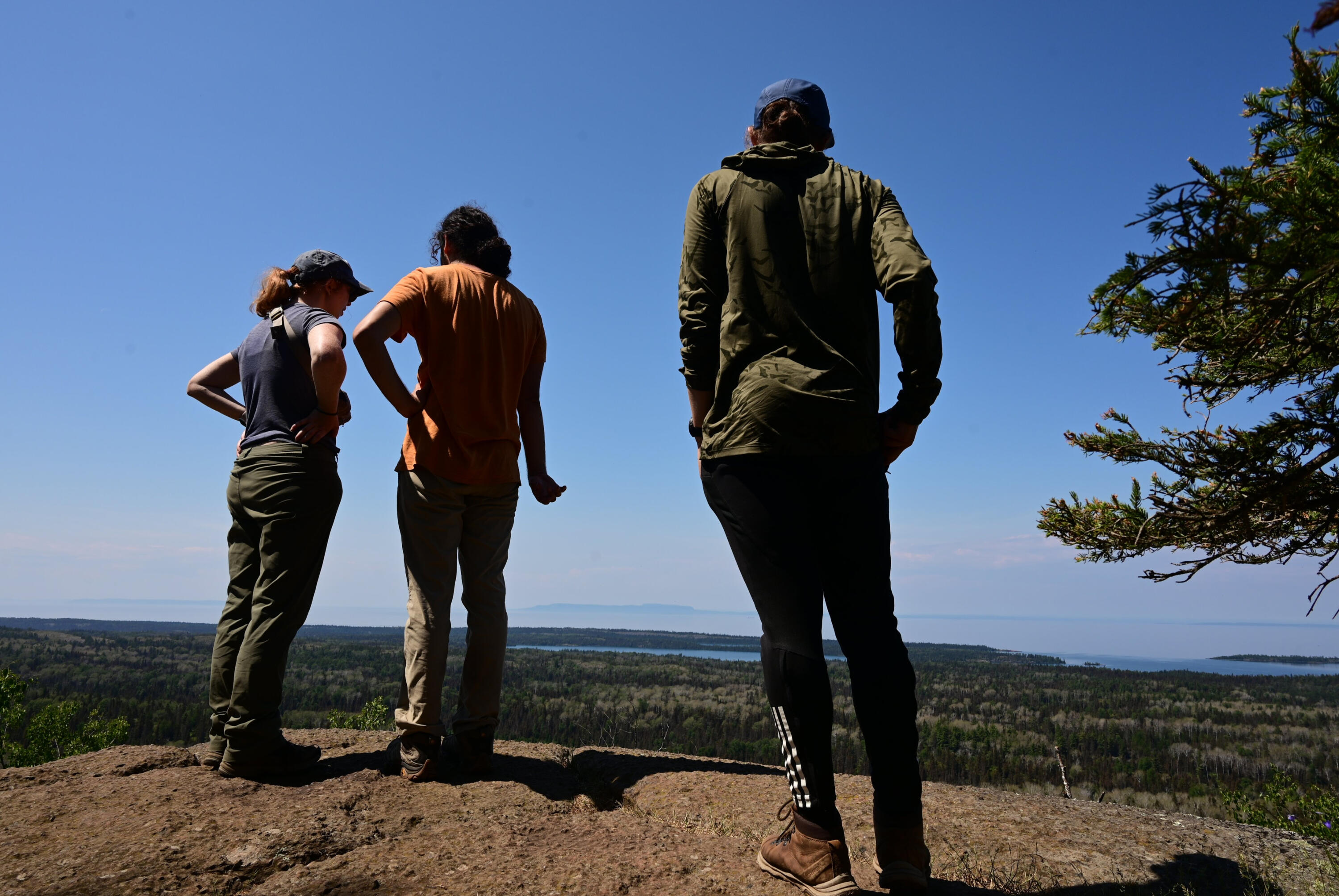 Three backpackers look off the cliff of Mt Franklin over the North side of Isle Royale towards Lake Superior and in the far distance, the Canadian Shore